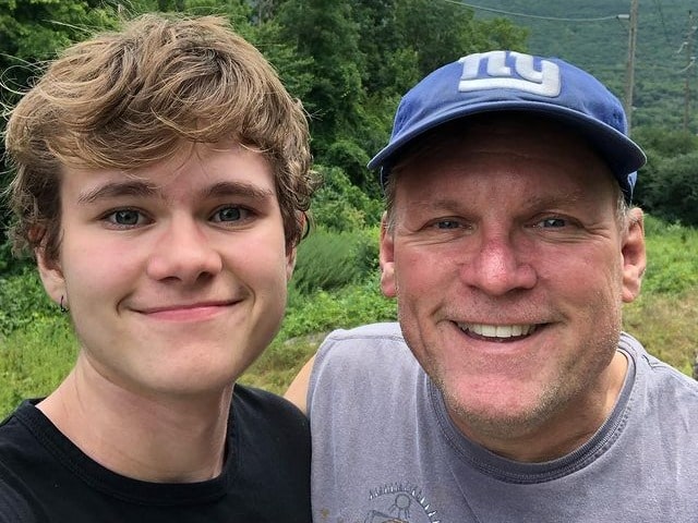 Writing about this photo, Isaiah is wearing a black T-shirt, with his dad  is wearing a grey half T-shirt and blue cap.